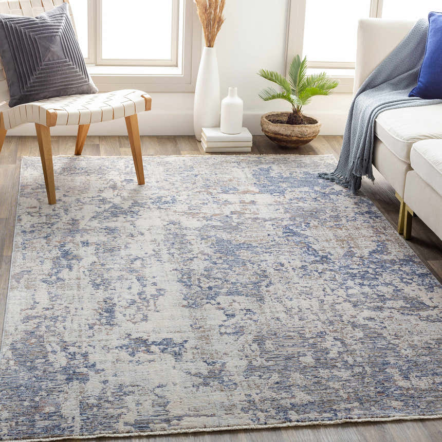 Living room scene with Broxbourne Area Rug in denim, taupe, and cream colors, styled with a white sofa and modern chair. Roomscene-Rectangle