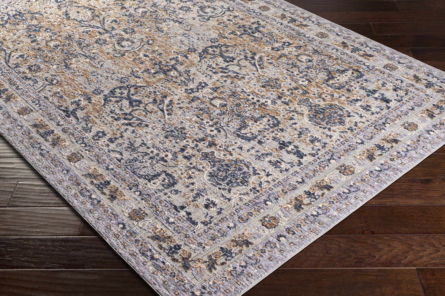Close-up of Barrie Area Carpet on dark wood floor. The rug has a traditional floral pattern in brown, charcoal, and cream. Corner