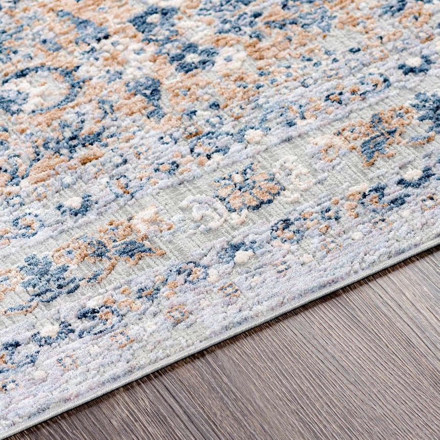 Close-up of the Barrie Area Carpet. Features a traditional pattern in cream, brown, and blue on a wood floor. Texture