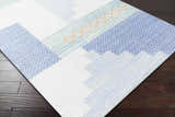 Close-up of the Bishopstoke Carpet, a hand-woven rug with blue, cream, and peach geometric patterns on a dark wood floor. Corner