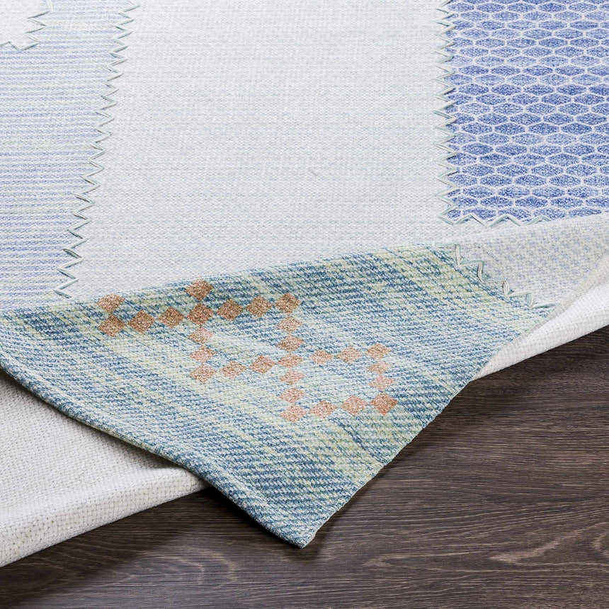 Close-up of Bishopstoke Carpet showing blue, cream, and peach tones with a hand-woven texture on dark wood floor. Fold