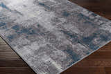 Close-up of a Bugho Area Rug - Clearance. Contemporary style rug in cream, gray, and denim on a dark wood floor. Corner