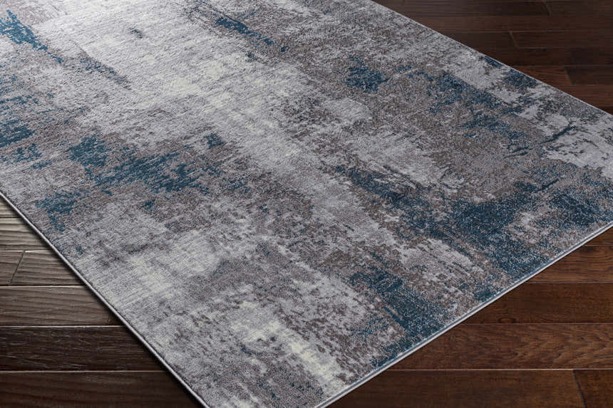 Close-up of a Bugho Area Rug - Clearance. Contemporary style rug in cream, gray, and denim on a dark wood floor. Corner