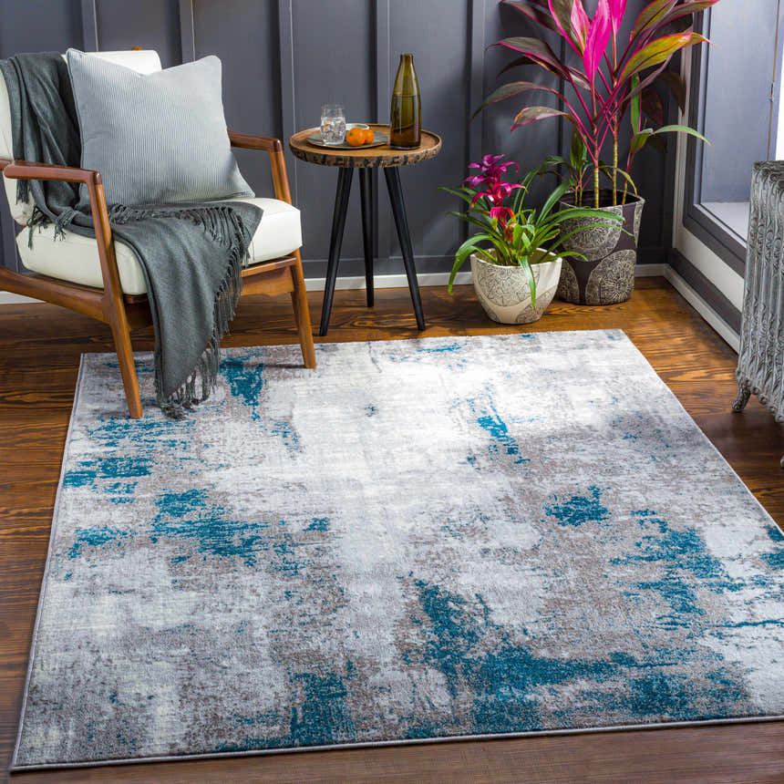 Living room scene with Bugho Area Rug in cream, gray, and teal. Modern chair, side table, and plants create a stylish space. Roomscene-Rectangle