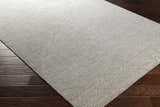 Close-up of the Bumpass Area Rug. Light sage and medium gray wool rug with a subtle geometric pattern on dark wood floors. Corner