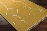 Close-up of the Bushra Area Rug; a yellow, hand-woven rug with a white geometric design and fringe detail. Corner