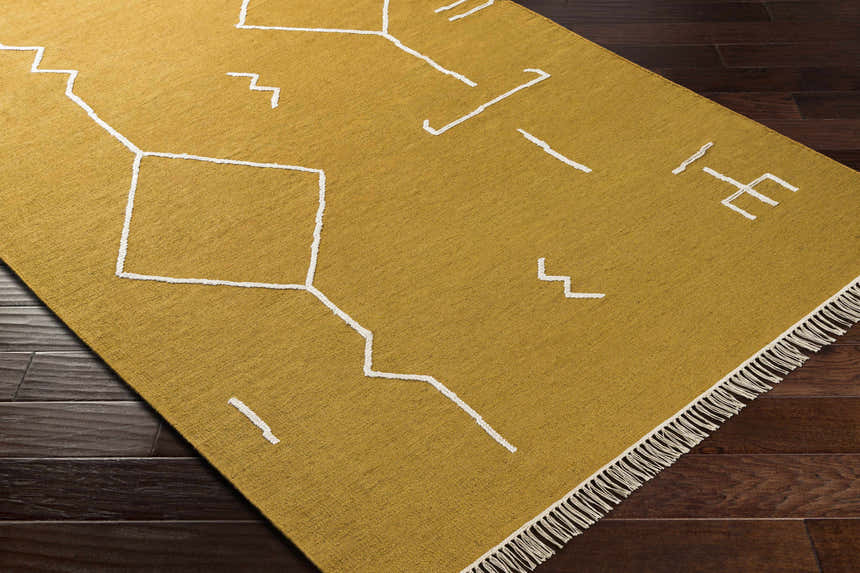 Close-up of the Bushra Area Rug; a yellow, hand-woven rug with a white geometric design and fringe detail. Corner
