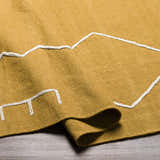 Close-up of the hand woven Bushra Area Rug in mustard yellow with a geometric white pattern. Fold