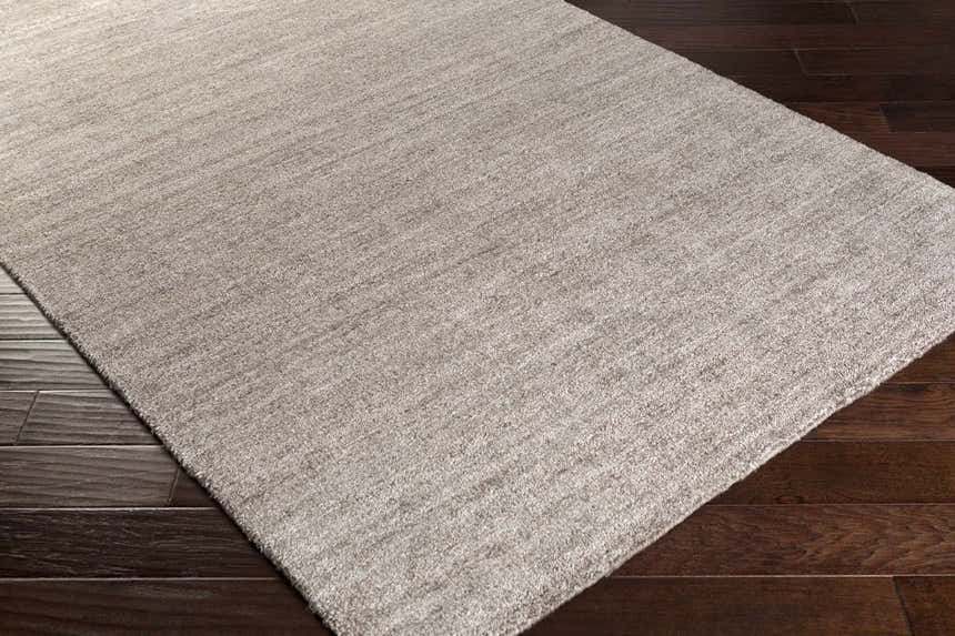 Close-up of the gray Buskirk Area Rug showing its hand-loomed texture and subtle contemporary design on dark wood flooring. Corner