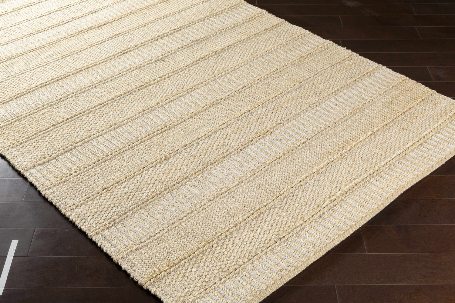 Close-up of the Bywong Area Rug. Beige and off-white jute rug with a hand-woven, striped texture. Corner