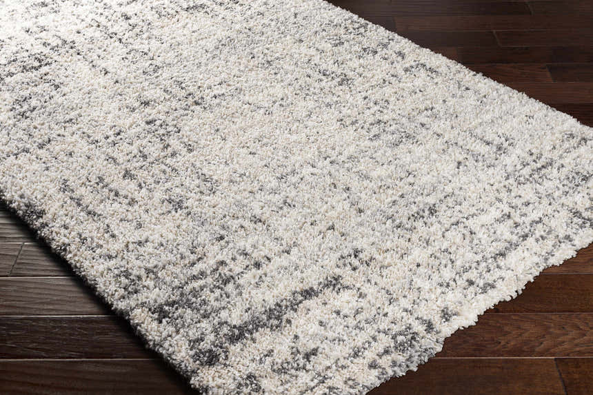 Close-up of the Calsib Area Rug, a shag rug in cream and black, on dark wood flooring. Corner