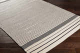 Close-up of the Calumpang Area Carpet. Beige cotton rug with black stripes and Southwestern diamond pattern. Hand woven texture. Corner