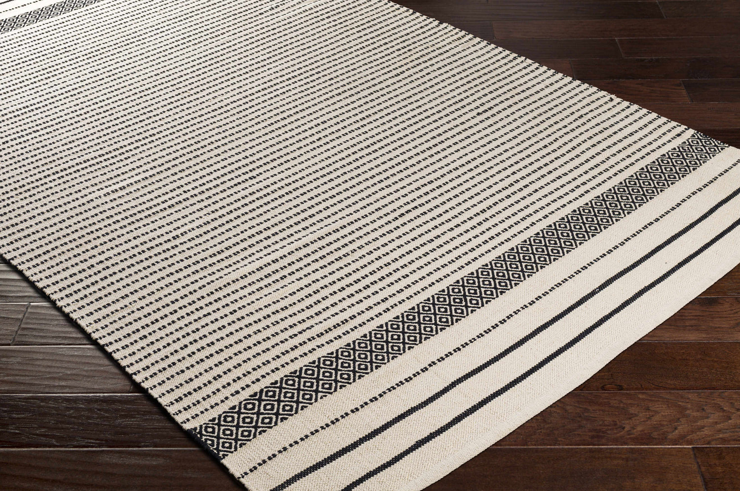 Close-up of the Calumpang Area Carpet. Beige cotton rug with black stripes and Southwestern diamond pattern. Hand woven texture. Corner