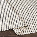 Close-up of the hand woven Calumpang Area Carpet. Beige cotton rug with black striped Southwestern design. Fold