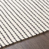 Close-up of the Calumpang Area Carpet. Beige rug with black, southwestern-style stripes on a wood floor. Texture