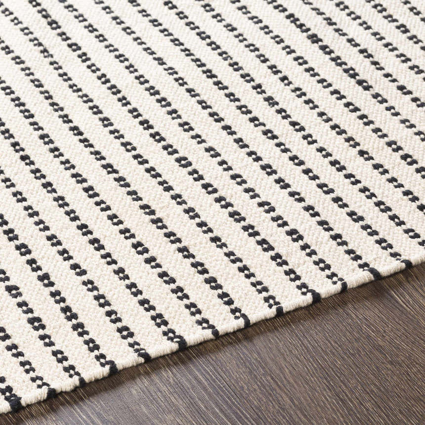 Close-up of the Calumpang Area Carpet. Beige rug with black, southwestern-style stripes on a wood floor. Texture