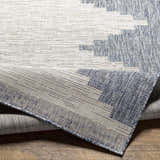 Close-up of Djugun Blue Outdoor Rug showing woven texture and geometric pattern in blue, gray, and off-white. Fold
