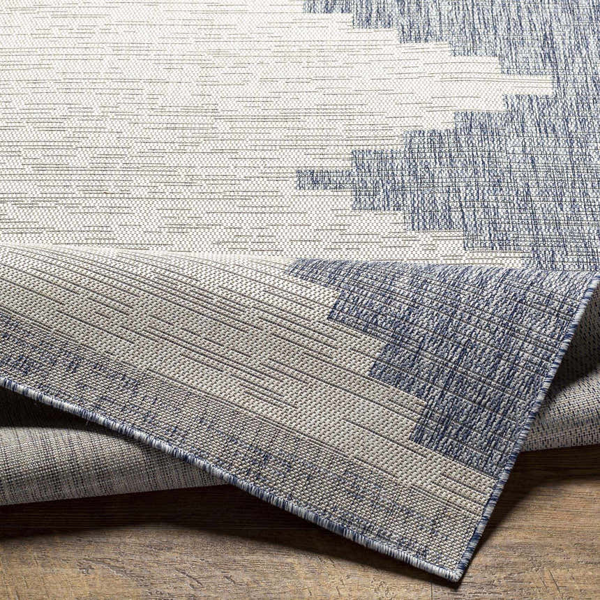 Close-up of Djugun Blue Outdoor Rug showing woven texture and geometric pattern in blue, gray, and off-white. Fold