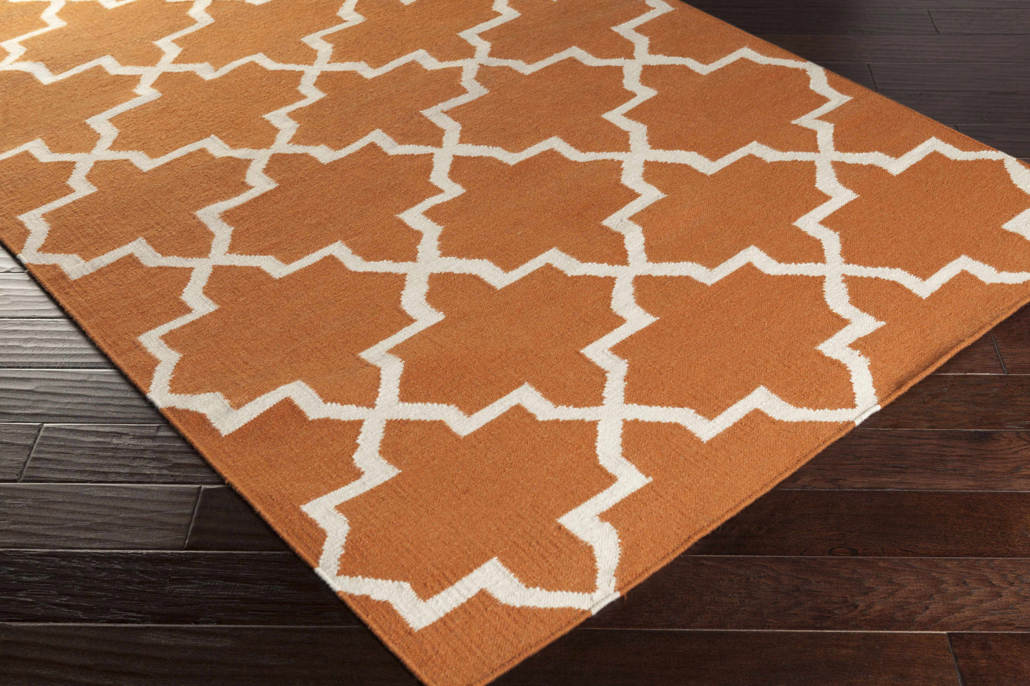 Close-up of the Canadys Area Rug. Hand-woven wool rug with a geometric white pattern on a burnt orange background. Corner