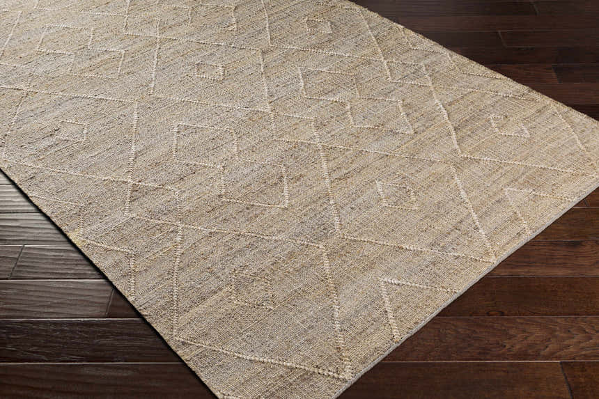 Close-up of the beige Carine Jute Area Rug showing its woven texture and geometric pattern on a dark wood floor. Corner