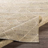 Close-up of the beige Carine Jute Area Rug showing its hand-woven texture and geometric pattern on a dark wood floor. Fold