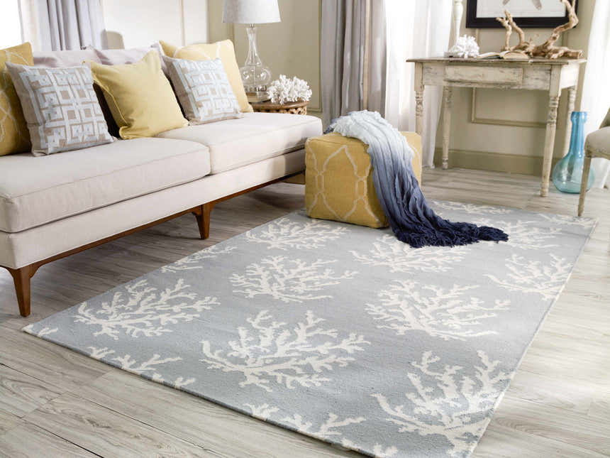 Living room scene with Carversville Ice Blue Botanical Wool Rug, ivory sofa, yellow ottoman, and coastal decor. Roomscene-Rectangle