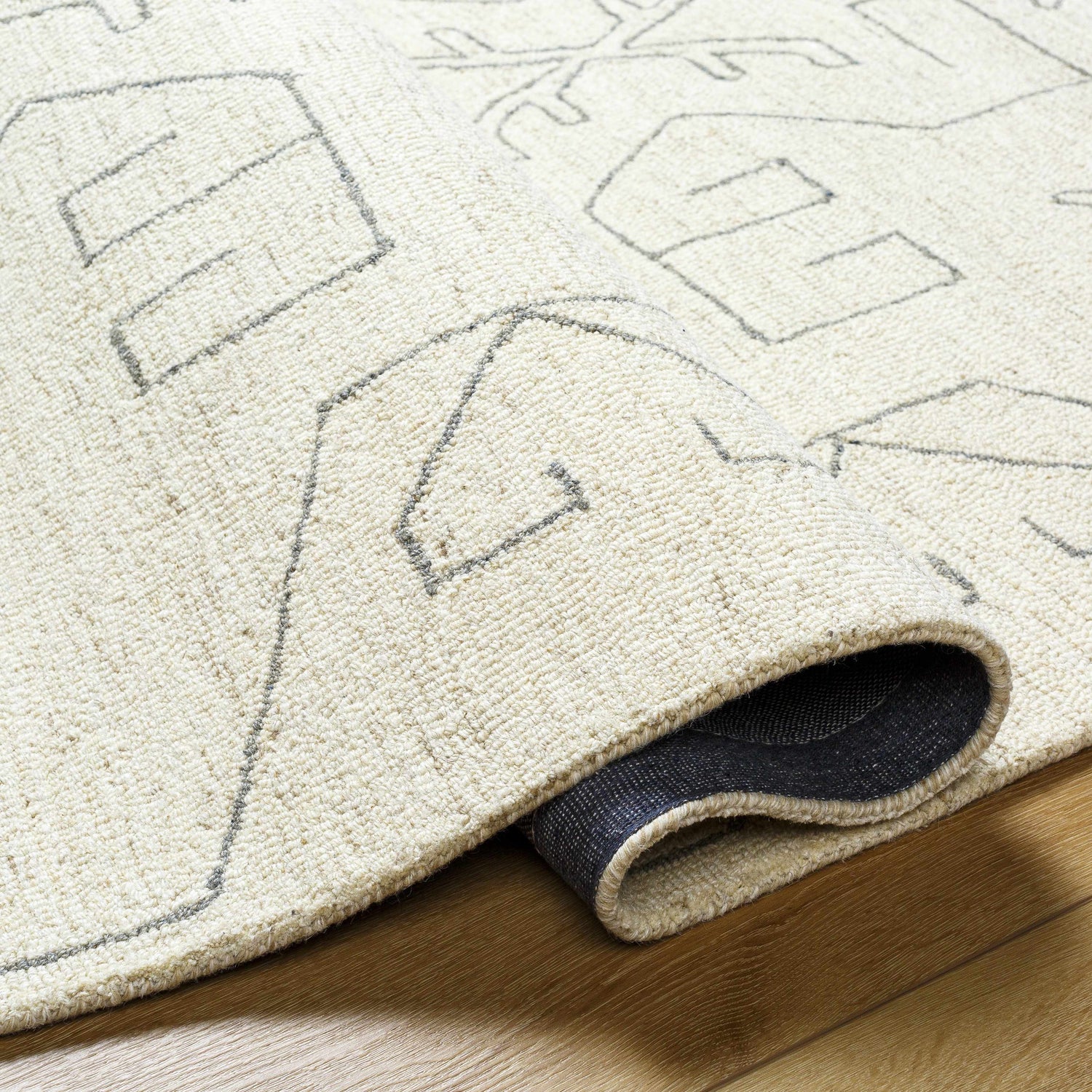 Close up of the hand-tufted Celia Area Rug, showcasing its wool texture and farmhouse-style geometric pattern in cream and gray. Fold