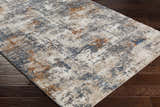 Close-up of Chetwynd Abstract Thick Rug on dark wood floor. Rug colors: blue, brown, cream, gray, beige. Abstract pattern. Corner