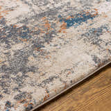 Close-up of the Chetwynd Abstract Thick Rug. Features blue, brown, cream, coral, and gray abstract pattern. Texture