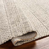 Close-up of the Cinco Luxe Rug showing its bone, driftwood, and gray tones, and textured, machine-woven construction. Fold