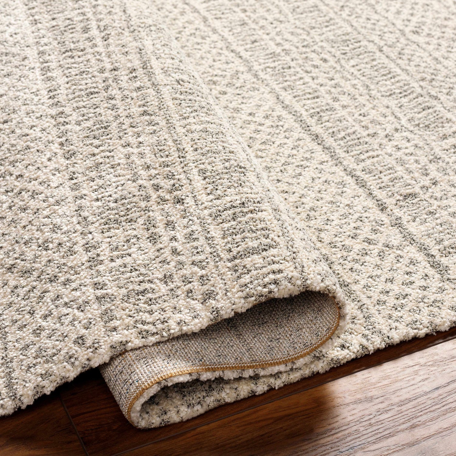 Close-up of the Cinco Luxe Rug showing its bone, driftwood, and gray tones, and textured, machine-woven construction. Fold