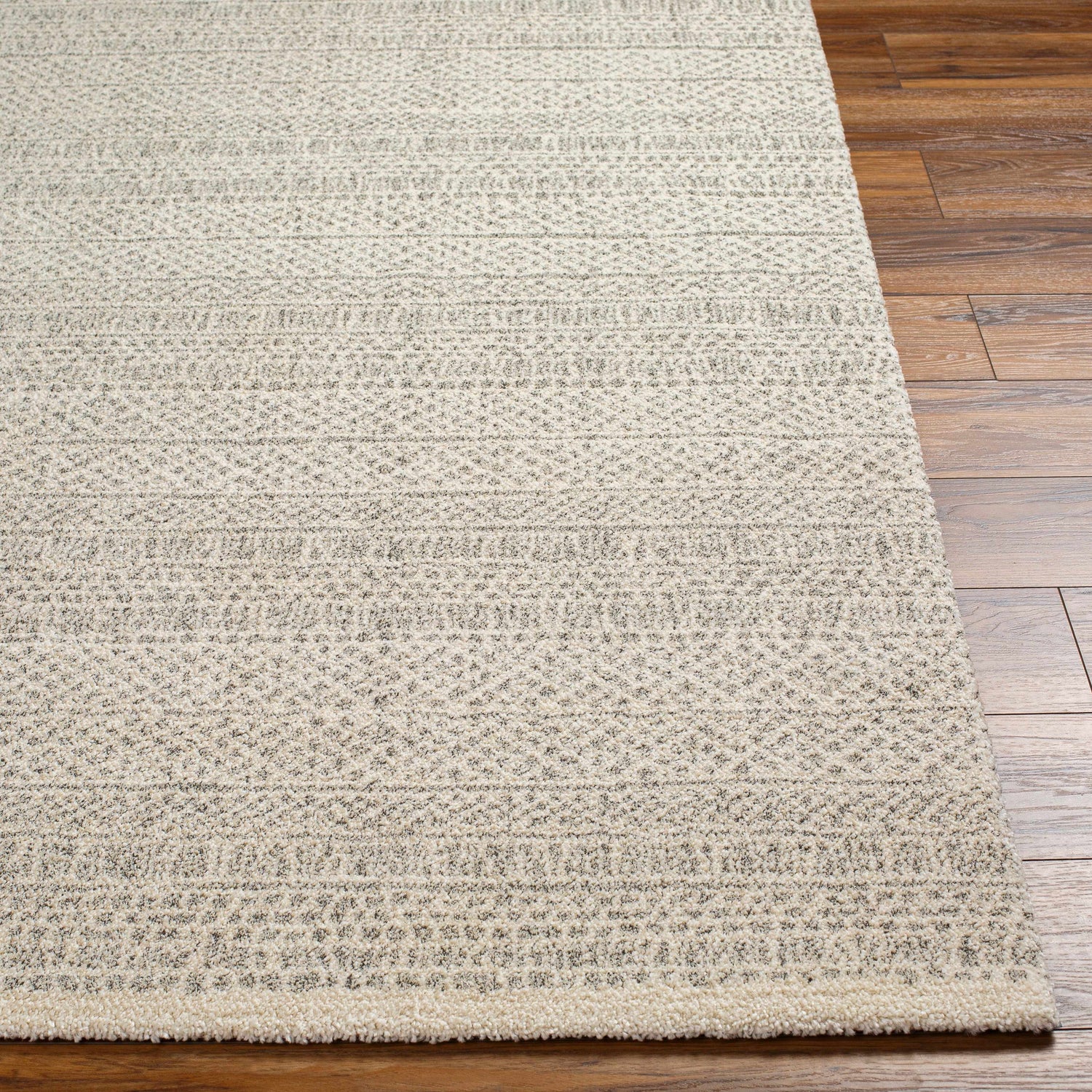 Close-up of the Cinco Luxe Rug showing its bone and gray geometric pattern and soft, textured pile on a wood floor. Front