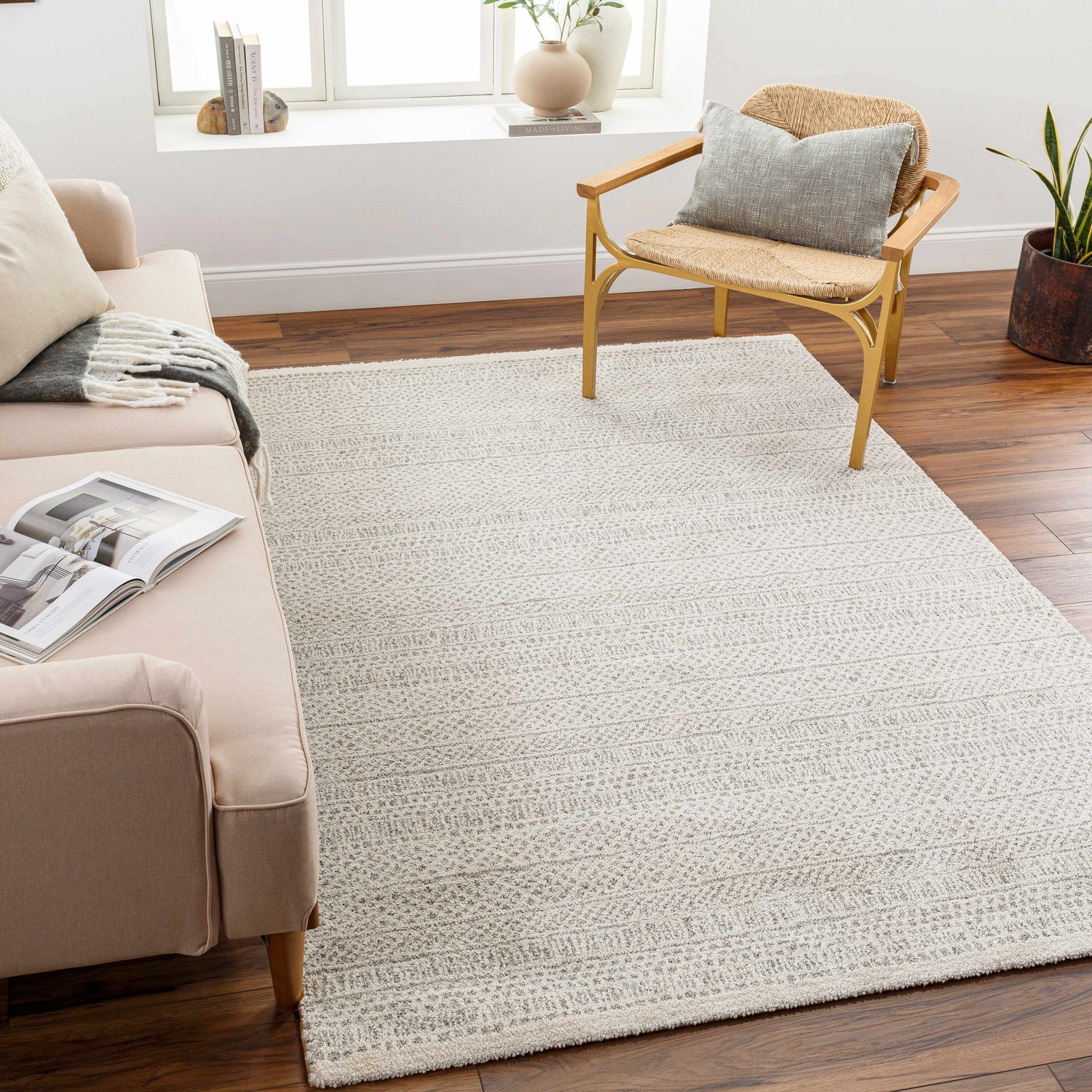 Living room scene with a bone-colored Cinco Luxe Rug, a beige sofa, and a straw chair on a dark wood floor. Roomscene-Rectangle