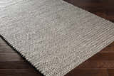 Close-up of the hand woven Cirencester Area Rug in ivory and medium gray on a dark wood floor. Corner