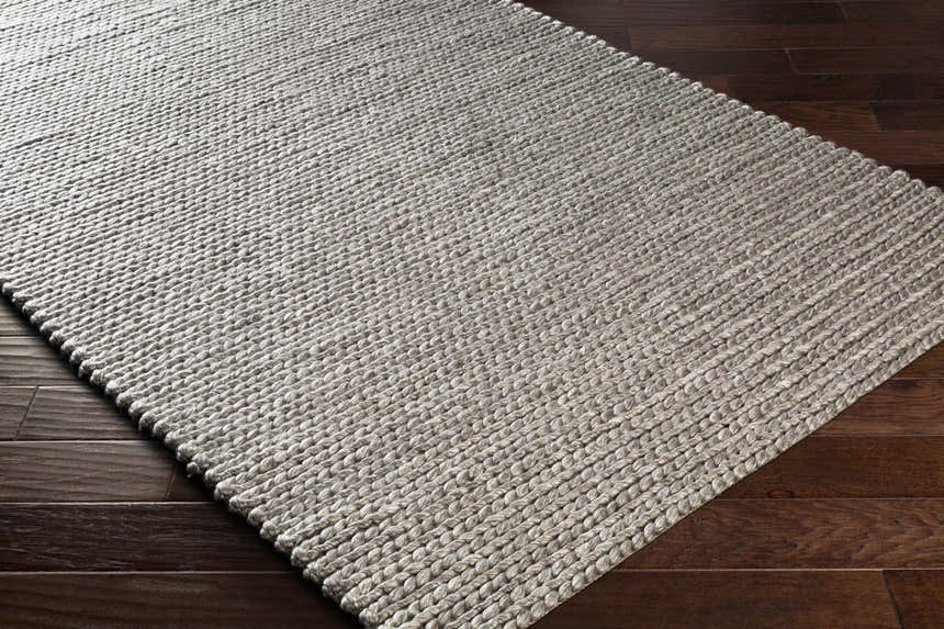 Close-up of the hand woven Cirencester Area Rug in ivory and medium gray on a dark wood floor. Corner