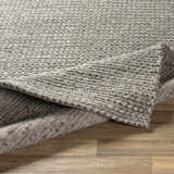 Close-up of the hand woven Cirencester Area Rug. The rug is ivory and medium gray with a chunky, braided texture. Fold