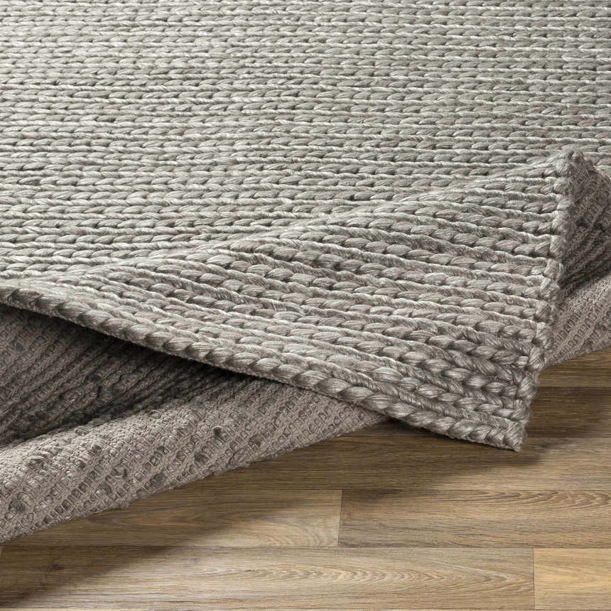 Close-up of the hand woven Cirencester Area Rug. The rug is ivory and medium gray with a chunky, braided texture. Fold