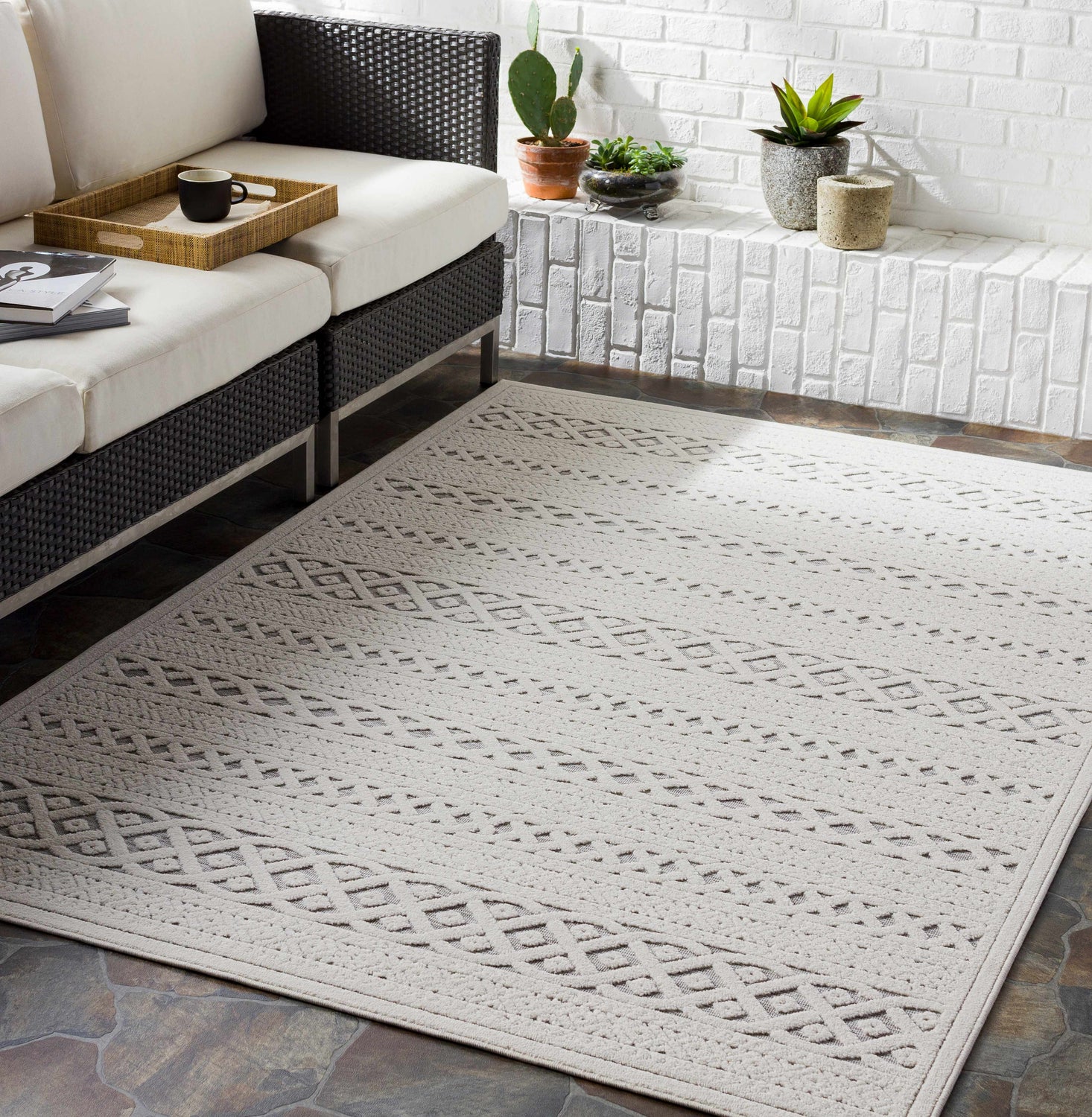 Living room scene with a Clenchwarton Textured Beige Rug, white sofa, brick wall, and potted plants. Roomscene-Rectangle