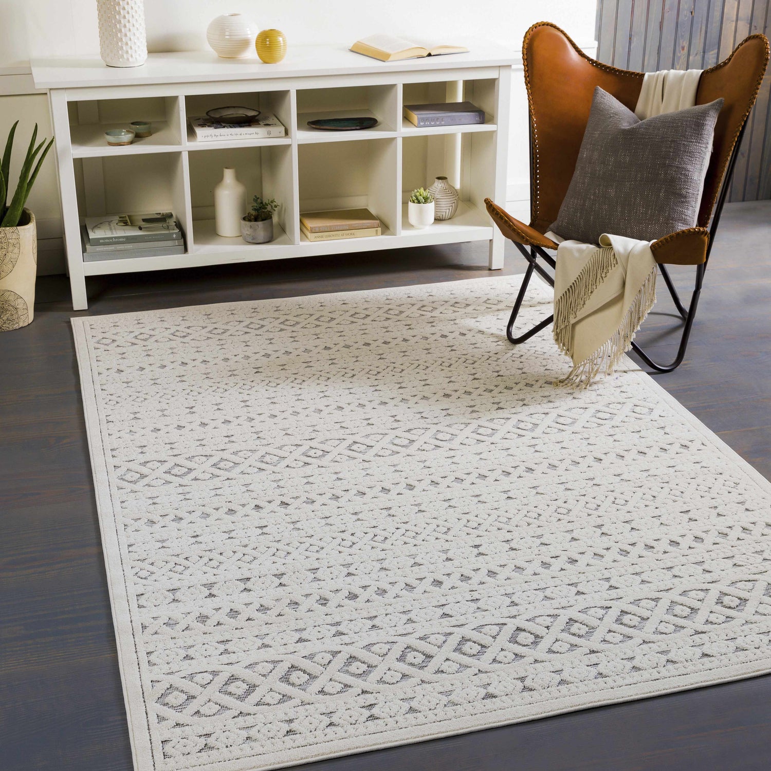 Living room scene with a Clenchwarton Textured Beige Rug, white shelving unit, and leather butterfly chair. Roomscene-Rectangle