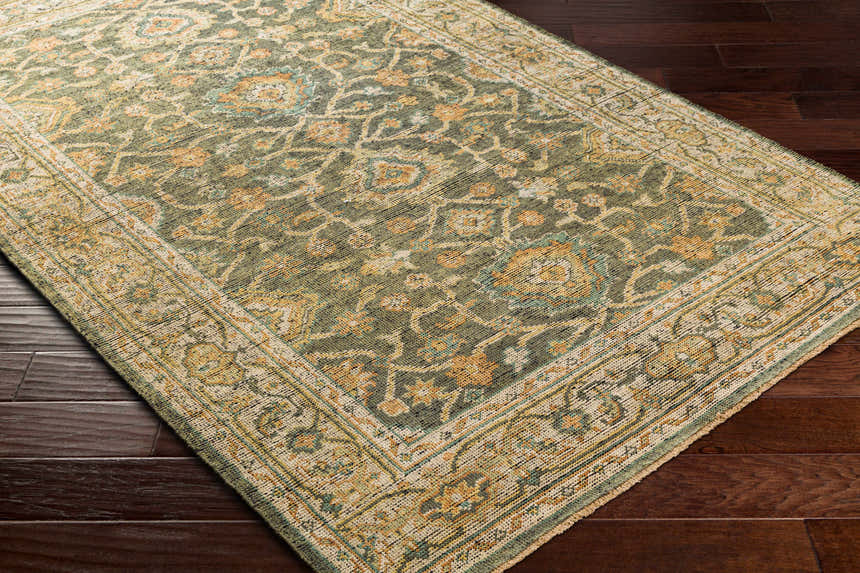 Close-up of the hand-knotted Clunes Area Rug. Traditional oriental design in grass green, yellow, beige, and brown on dark wood floors. Corner