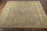 Close-up of the hand-knotted Clunes Area Rug in black, brown, sage, and yellow on a dark wood floor. Oriental rug style. Front