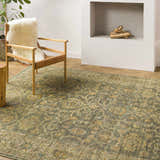 Living room scene with Clunes Area Rug in sage, yellow, and beige. A chair with a sheepskin throw sits on the rug near a fireplace. Styleshot