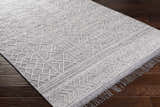 Close up of Gray Clintwood Wool Tassel Carpet on dark wood floor. Bohemian style rug with geometric pattern. Corner