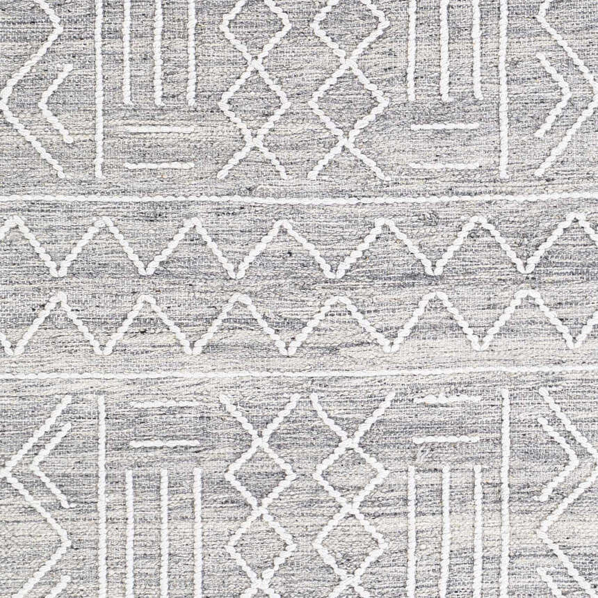 Close-up of Gray Clintwood Wool Tassel Carpet showing geometric white pattern on charcoal, cream, and oatmeal woven texture. Swatch