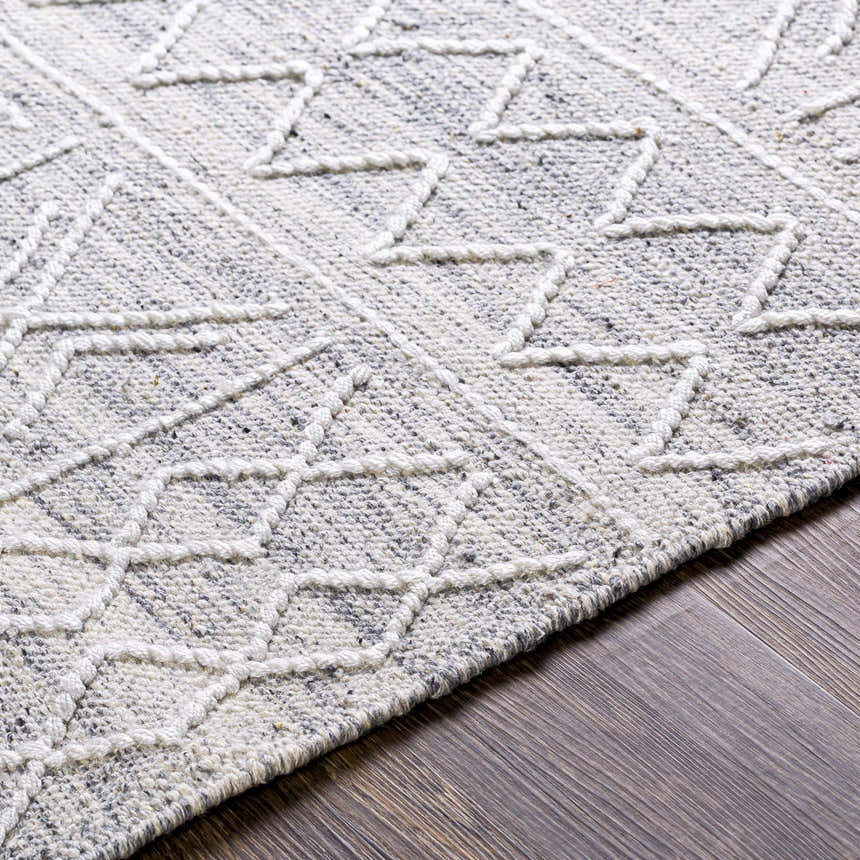 Close-up of Gray Clintwood Wool Tassel Carpet showing geometric pattern and textured weave in charcoal, cream, oatmeal, and white. Texture