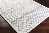 Close-up of the shag Clarkia Area Rug, a white rug with a gray geometric pattern, on a dark wood floor. Corner