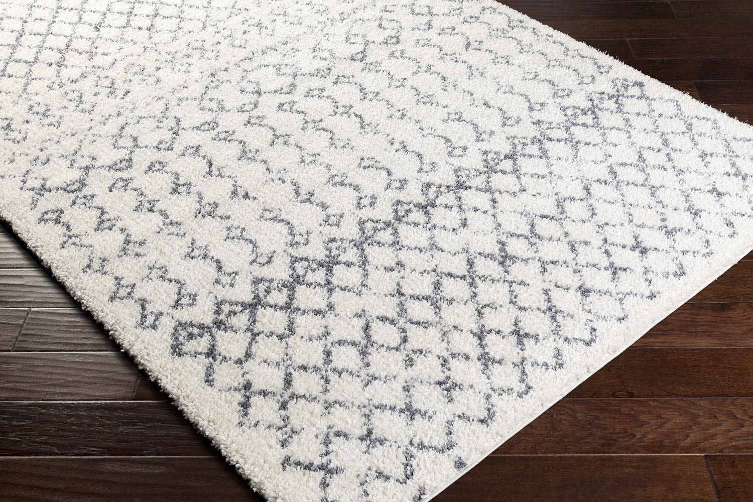 Close-up of the shag Clarkia Area Rug, a white rug with a gray geometric pattern, on a dark wood floor. Corner