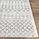 Close-up of the shaggy Clarkia Area Rug. Features a geometric gray and white pattern on a wood floor. Front