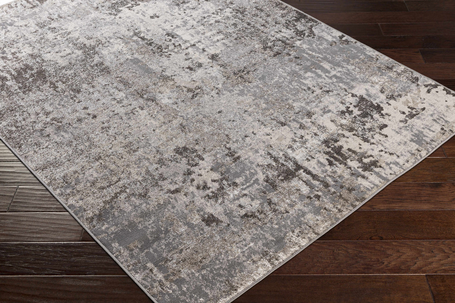 Close-up of the Calvinia Area Rug showing charcoal, gray, and light gray abstract pattern on dark wood floor. Corner
