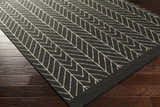 Close-up of the Clymer Wool Rug. Black rug with off-white geometric herringbone pattern on dark wood floors. Corner